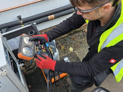 HVAC technician using gauges to check refrigeration or air conditioning system pressure outdoors.
