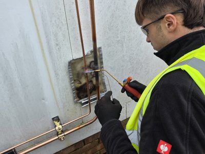 HVAC technician performing pipework repair with a blowtorch on an outdoor unit.